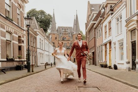 Rennend als getrouwd stel door de straten in hartje Kampen bij de broederpoort. foto: Wilco de Haan Fotografie, trouwfotograaf Winschoten, Groningen